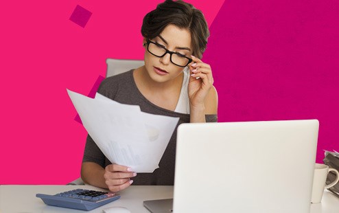 Donna intenta a leggere dei documenti con pc e calcolatrice sulla scrivania.
