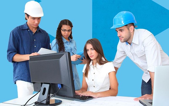 Diversi colleghi, un paio hanno un casco in testa, riuniti intorno a una collega alla scrivania che lavora davanti al PC, un altro ha in mano un tablet.