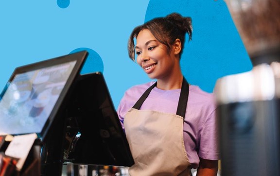 Ragazza sorridente con grembiule alla cassa di un'attività commerciale.