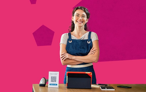 Ragazza sorridente con grembiule davanti a un tavolo con tablet e qrcode per pagamenti.