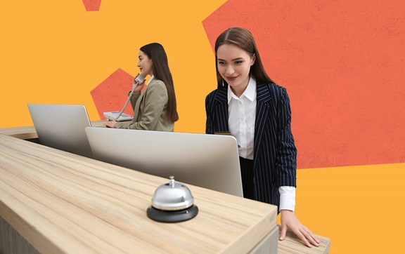 Coppia di donne impegnate alla reception, una al telefono e una sorridente davanti a un monitor.