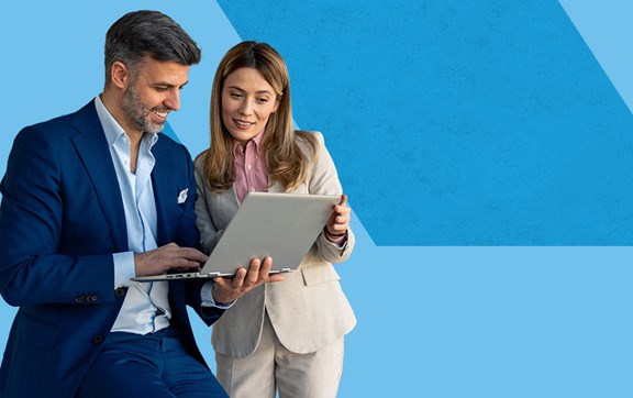 Uomo brizzolato con completo e donna sorridenti che guardano insieme su un pc portatile.